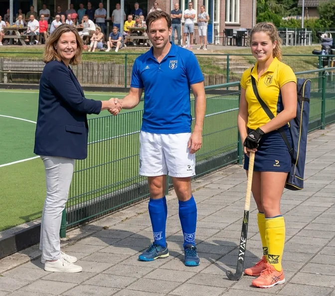 Een bestuurslid geeft bij het clubhuis een hand aan twee leden die net zijn aangekomen